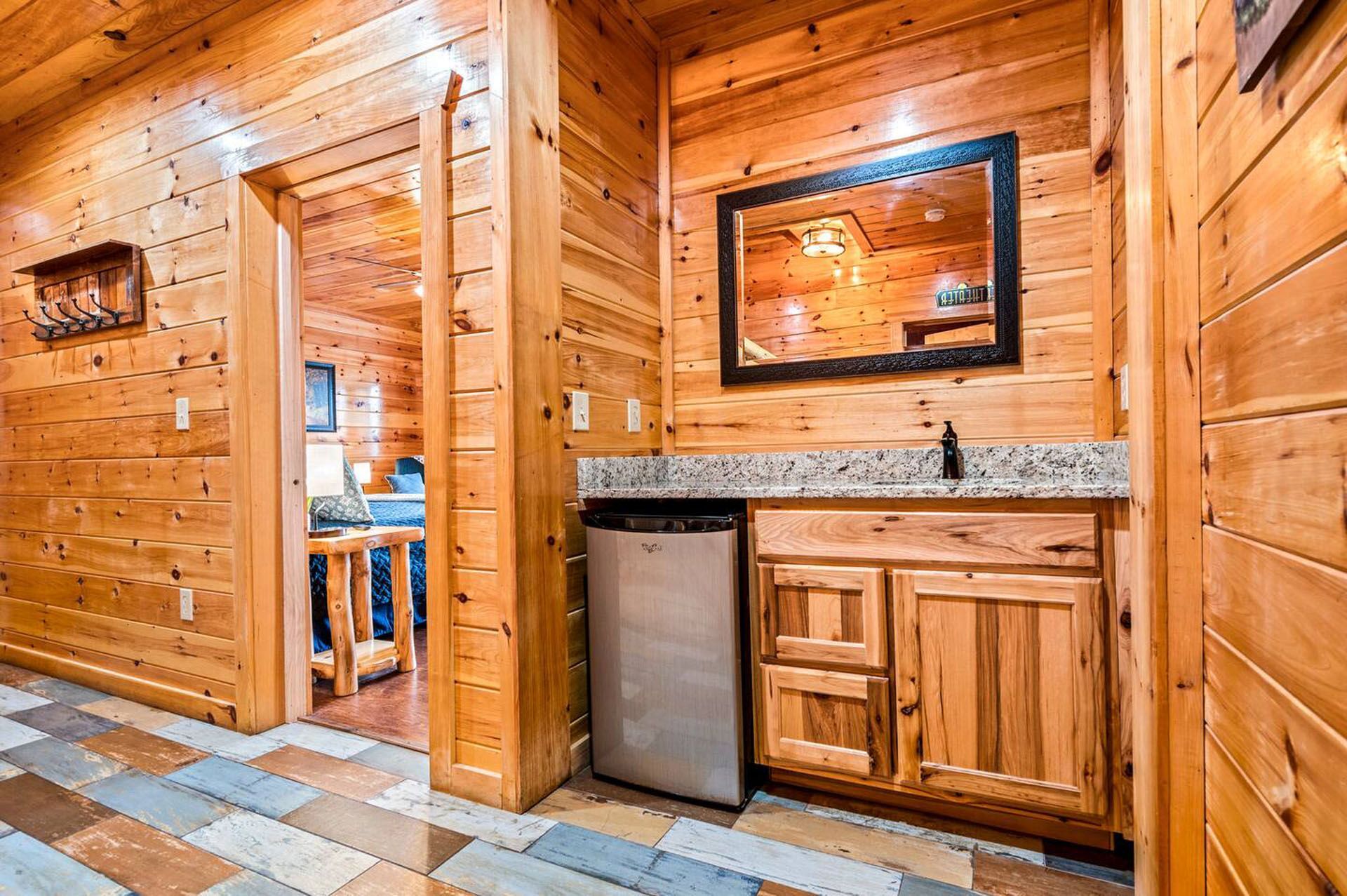 Wooden cabin interior with a mini-fridge, cabinets, mirror, and a doorway to another room.