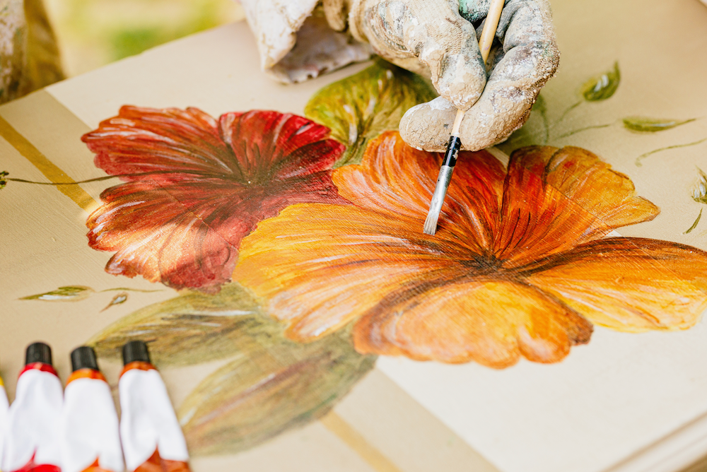 A person is painting a flower with a brush on a table.
