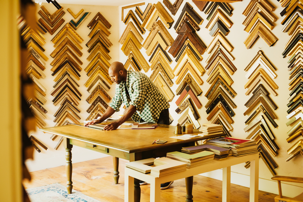 A man is sitting at a table in front of a wall of wooden frames.