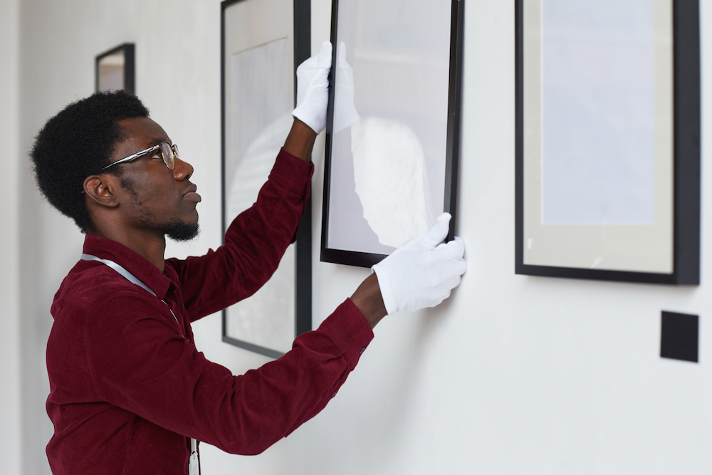 A man wearing white gloves is hanging a picture on a wall.