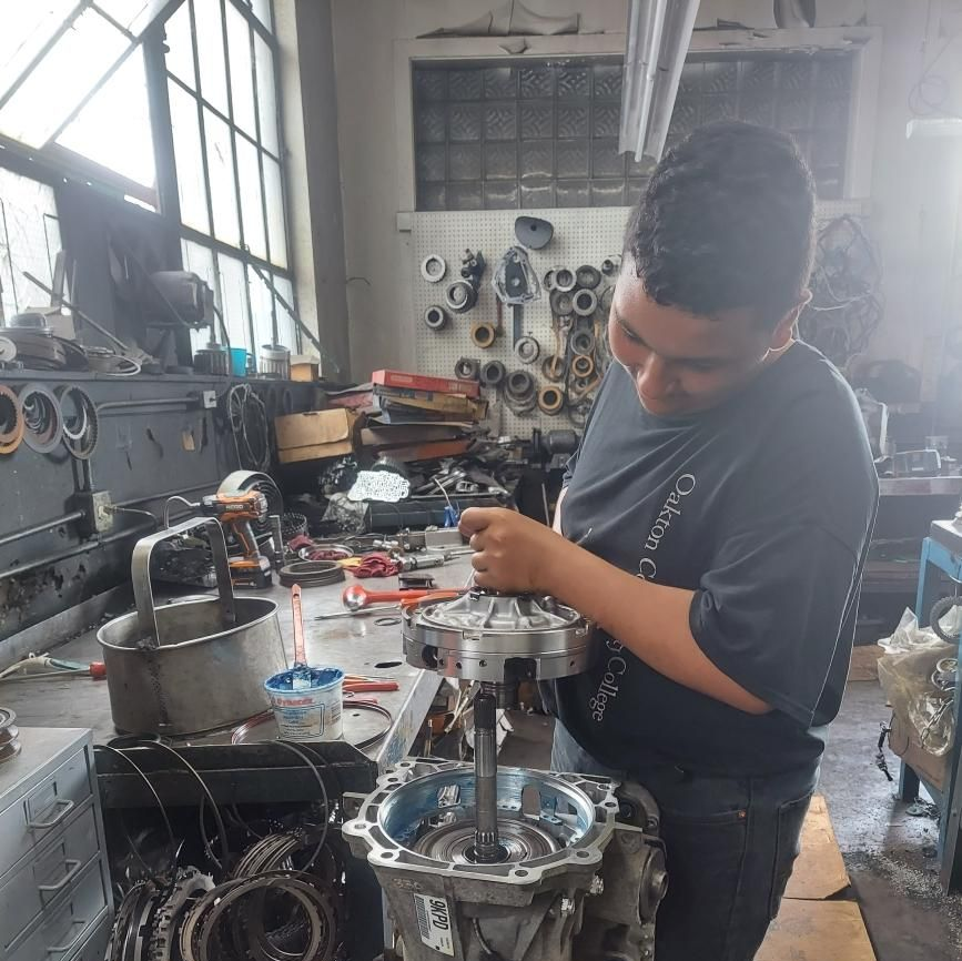 AAMCO mechanic showing a man a tablet while working on a car engine in an AAMCO garage.