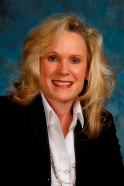 A woman in a black jacket and white shirt is smiling for the camera.
