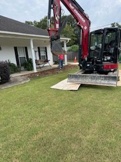 A red and black excavator is sitting in front of a house.