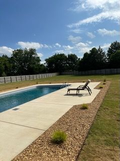 A large swimming pool is surrounded by lawn chairs and gravel.