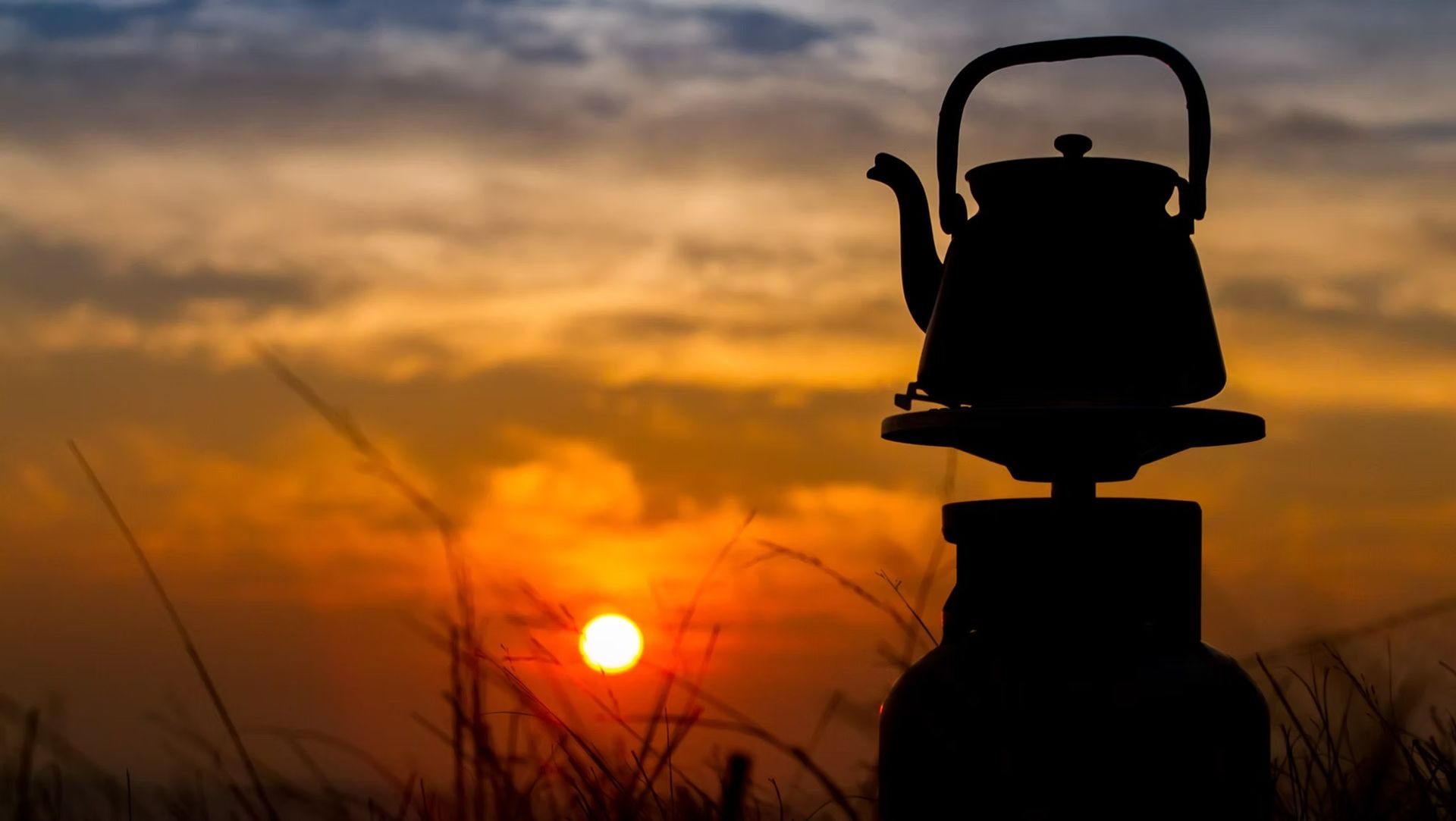 A silhouette of a tea kettle sitting on top of a stove at sunset.