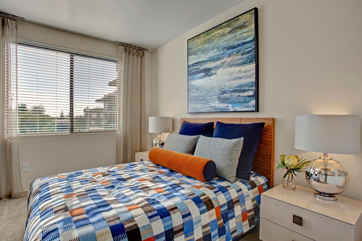 A bedroom with a bed , nightstand , lamps and a painting on the wall.