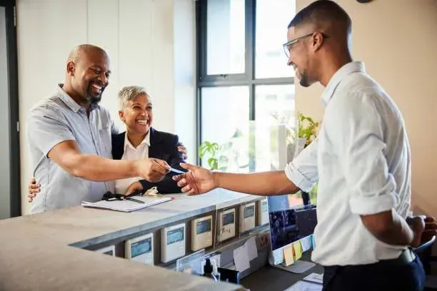 A man is giving a credit card to another man at a hotel counter.