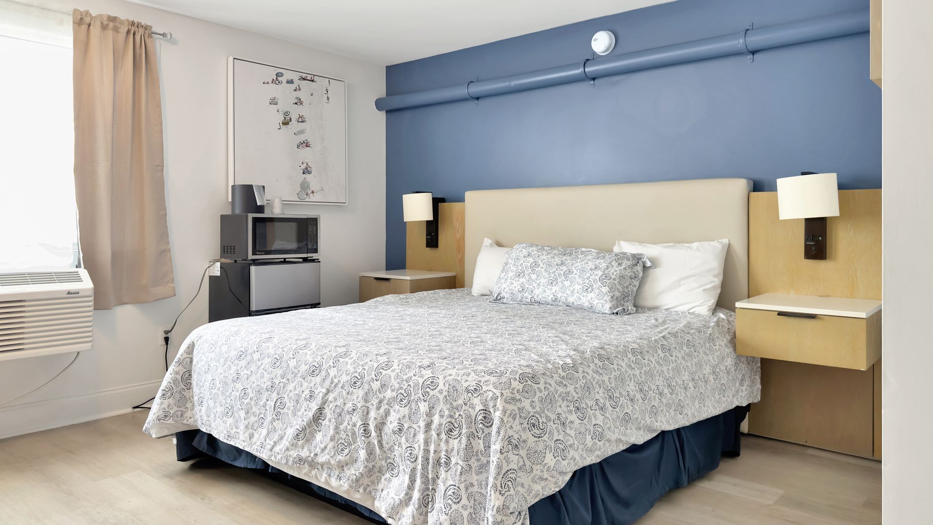 Bedroom with bed, bedside tables, and blue accent wall; small appliances near the window.