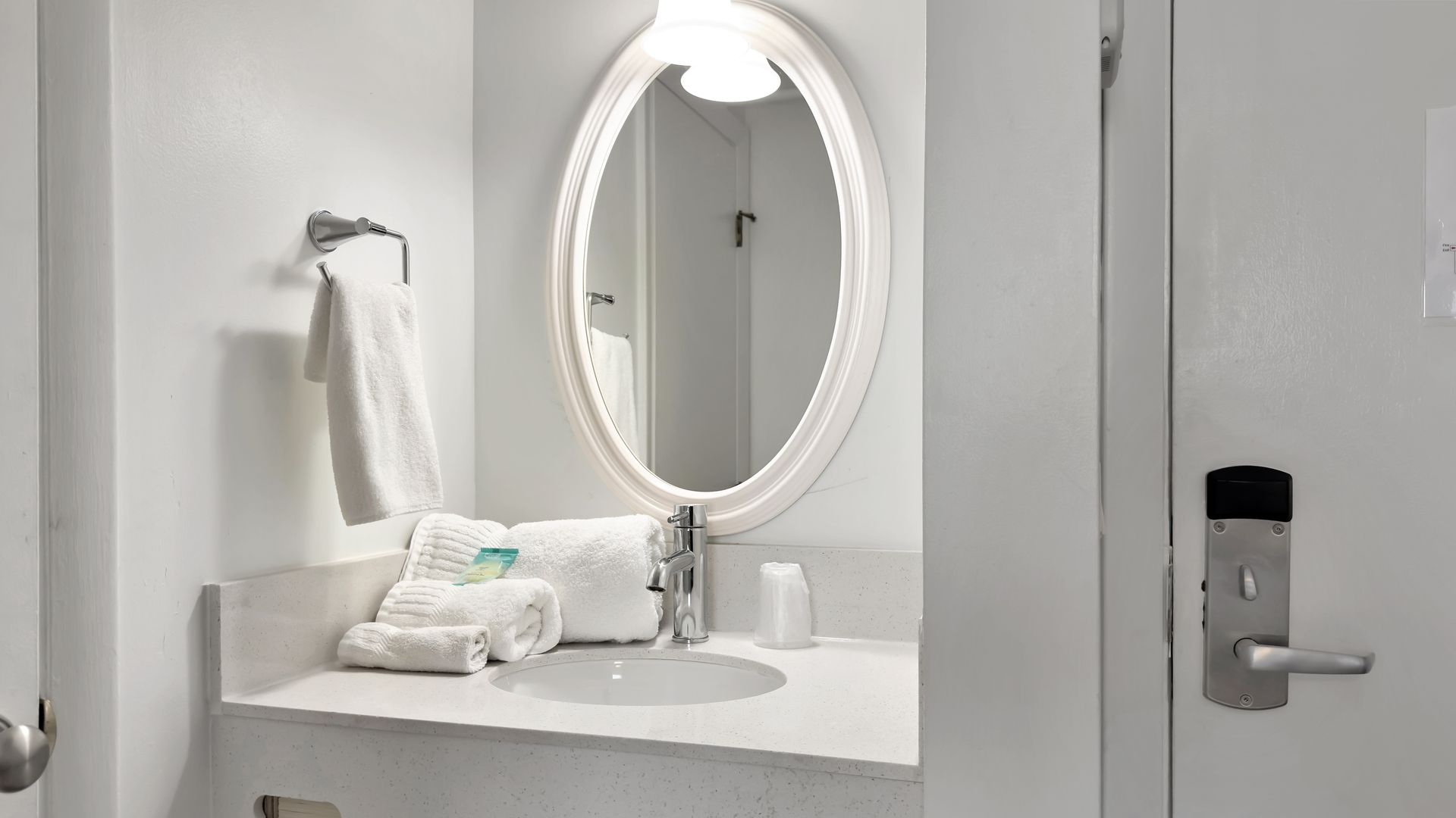 Bathroom with white walls, sink, oval mirror, and folded towels on a countertop.