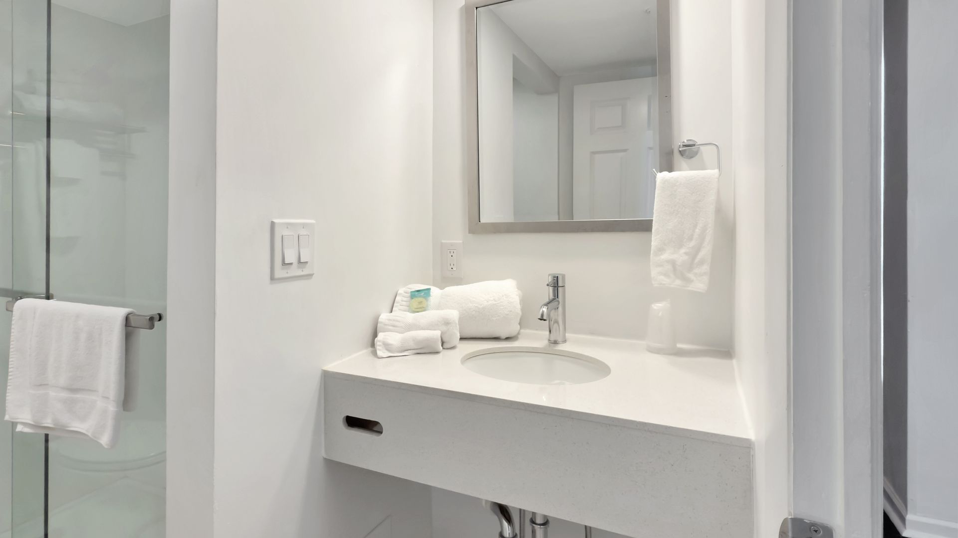 Bright white bathroom with a sink, mirror, and shower. White towels are visible.