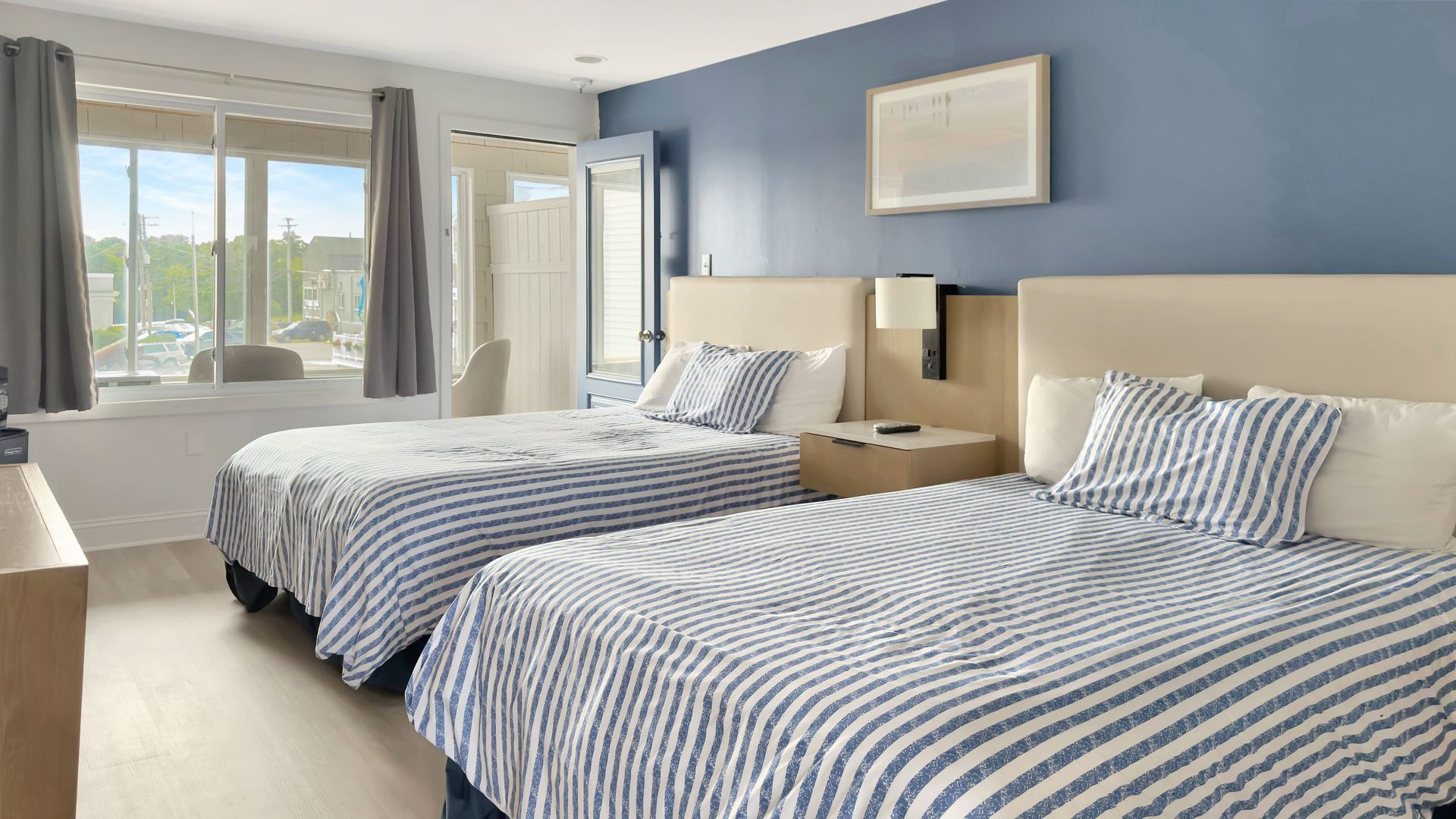 Hotel room with two beds, blue and white striped comforters, blue walls, and large window.