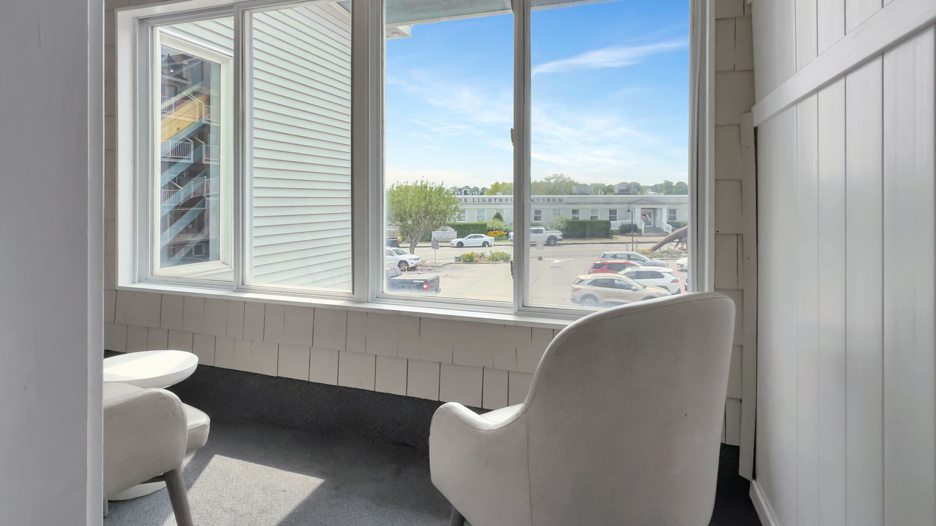 White armchair beside window, view of parking lot. Bright sunlight.