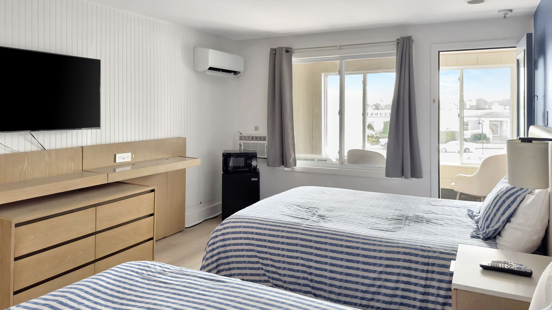 Hotel room with two beds, TV, small fridge, and window overlooking a city view.