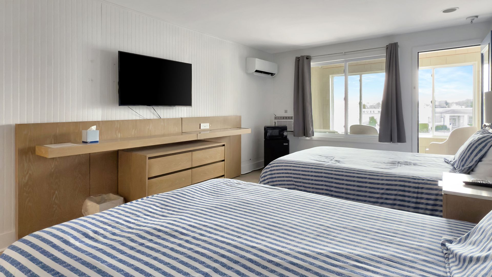 Two beds in a light-filled hotel room with a view of the ocean, and a TV.