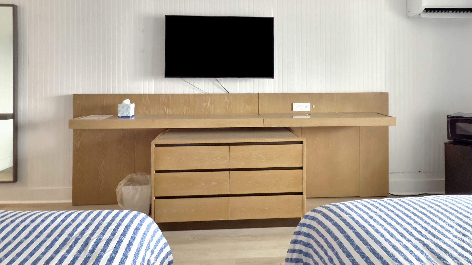 Two beds in a room with a dresser, TV, and a white wall.