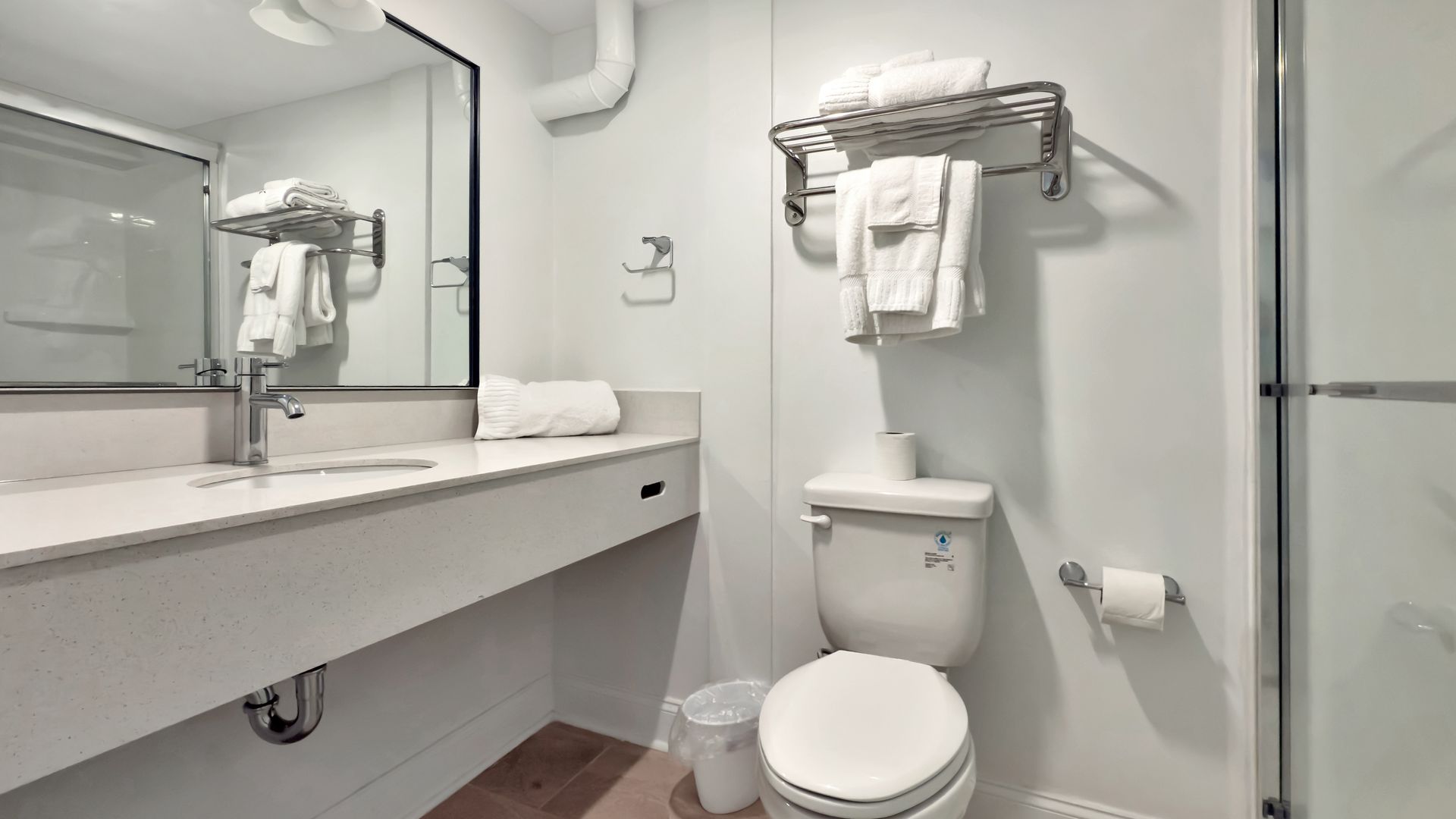 Bathroom with white sink, toilet, and towels, and a shower with a glass door.