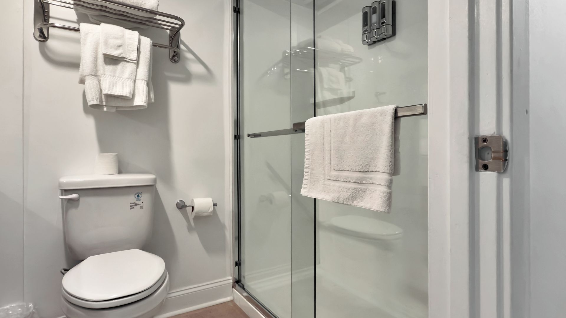 Bathroom with toilet, shower with glass door, and towel rack with white towels.