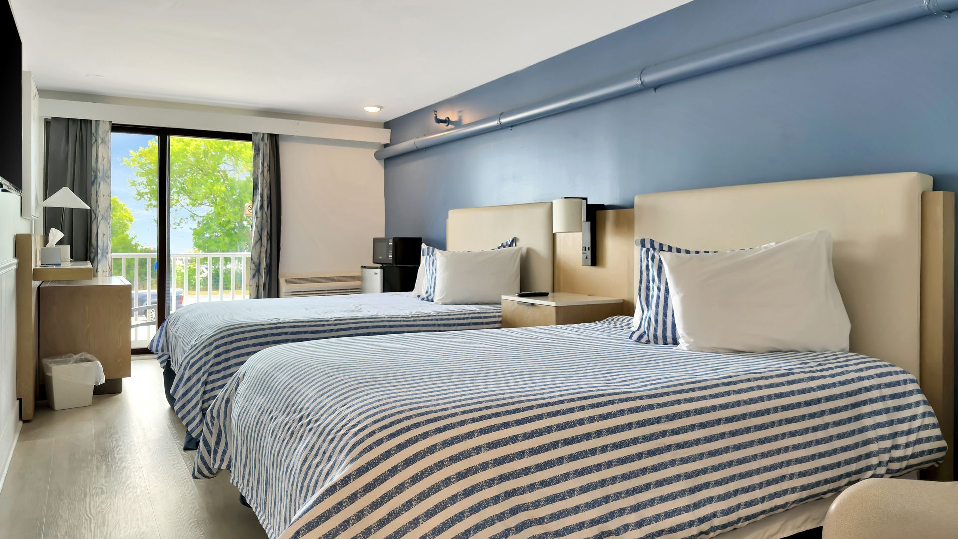 A hotel room with two twin beds with blue and white striped bedding, a balcony, and blue walls.