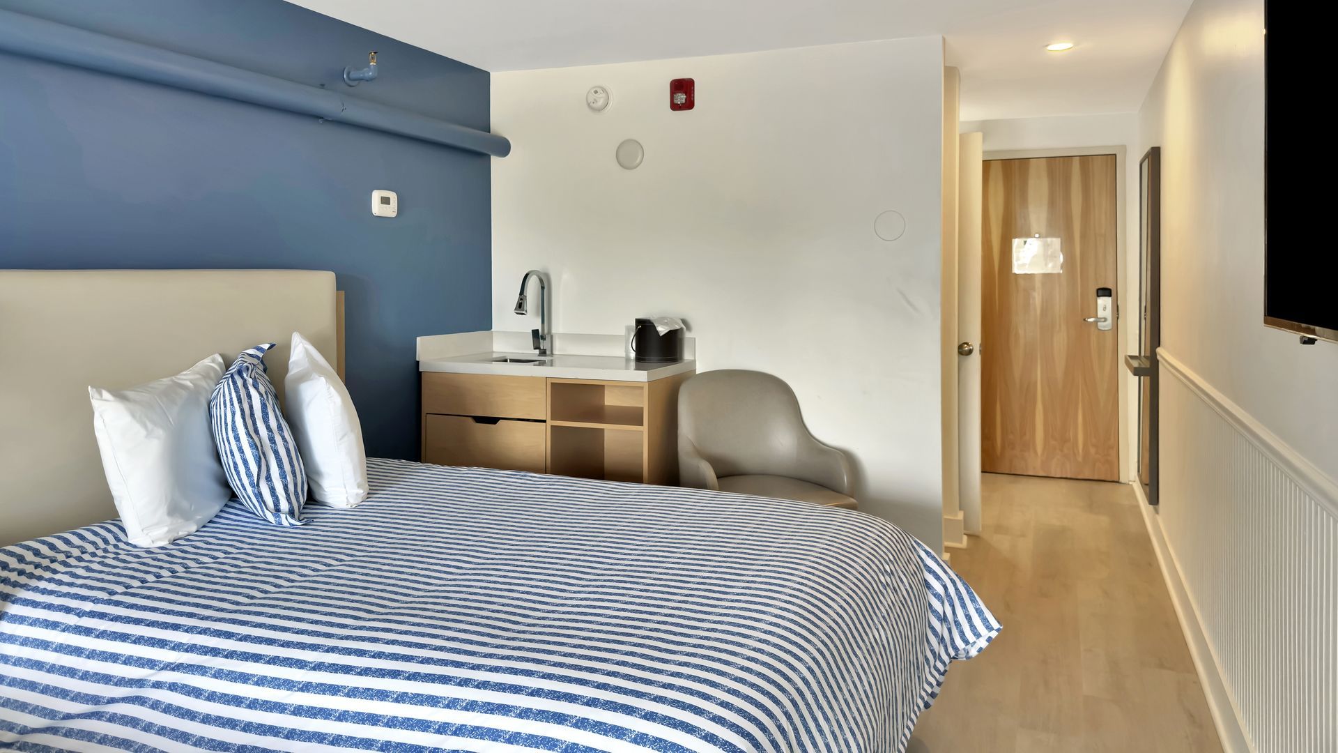A hotel room with a bed, sink, chair, and door. Blue and white color scheme.