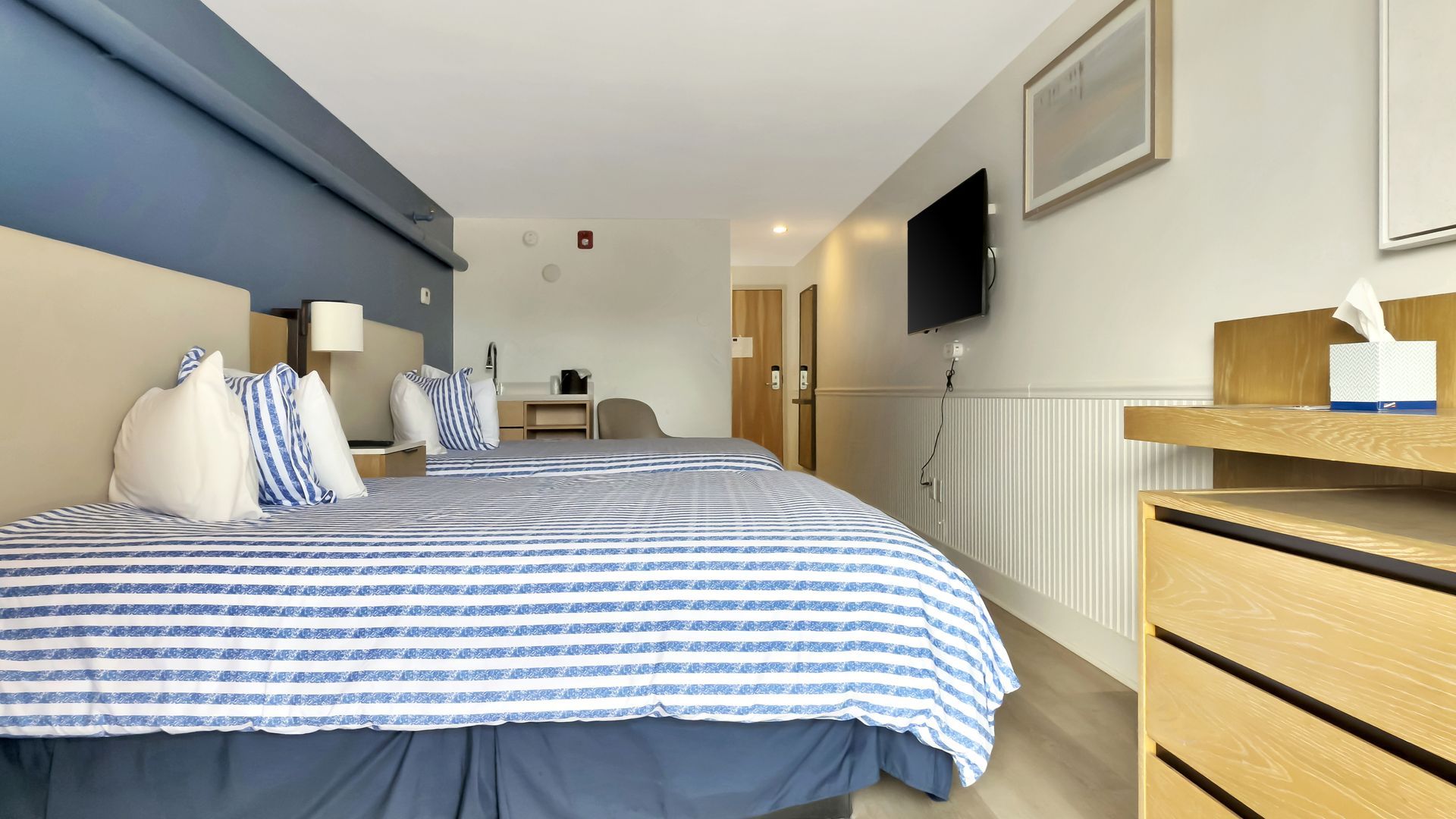 Hotel room with two beds, blue and white striped bedding, and a mounted television.