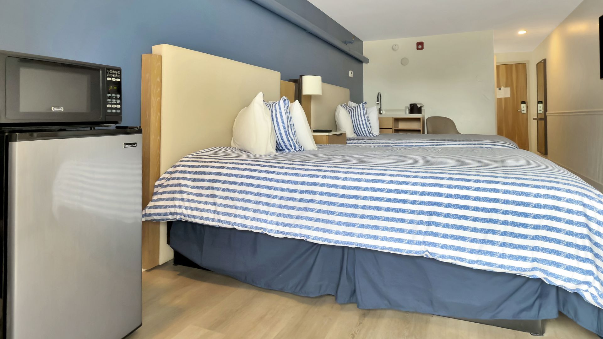 Hotel room with two double beds, microwave, mini-fridge, and blue and white striped bedding.