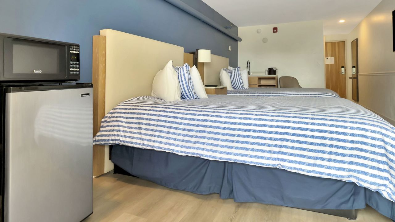 Hotel room with two beds, microwave, and mini-fridge. Blue and white striped bedspreads.