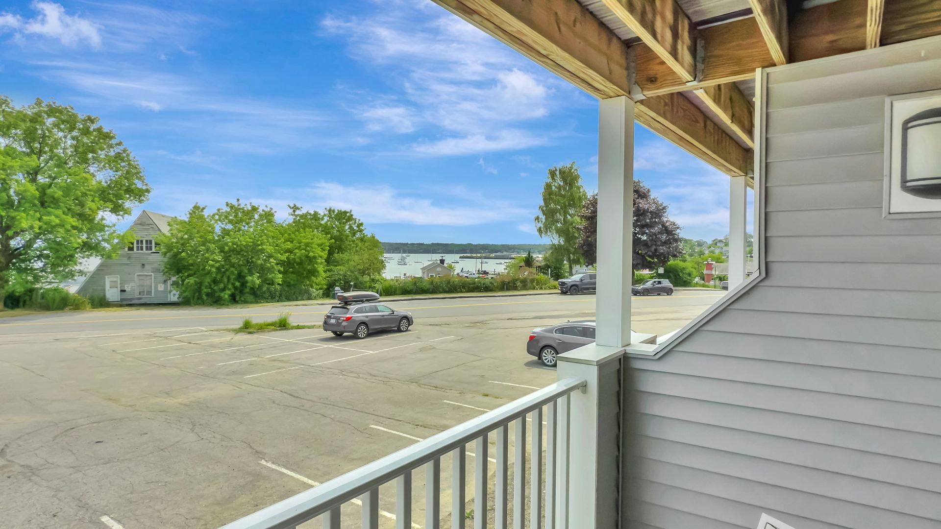 View from a covered balcony overlooking a parking lot and waterfront under a blue sky.