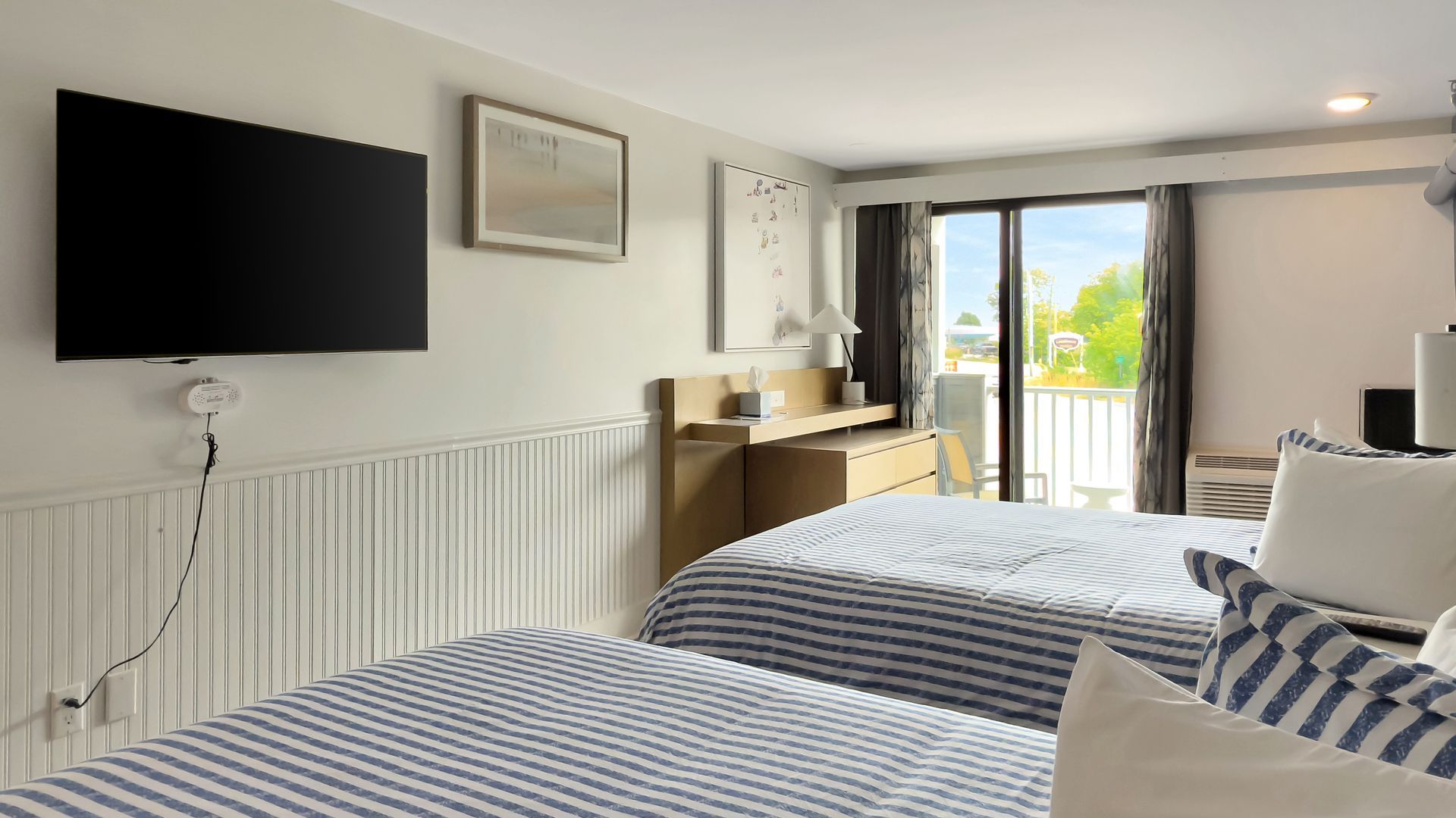 Bedroom with two twin beds, a TV, and a balcony door. Beds have blue and white striped covers.