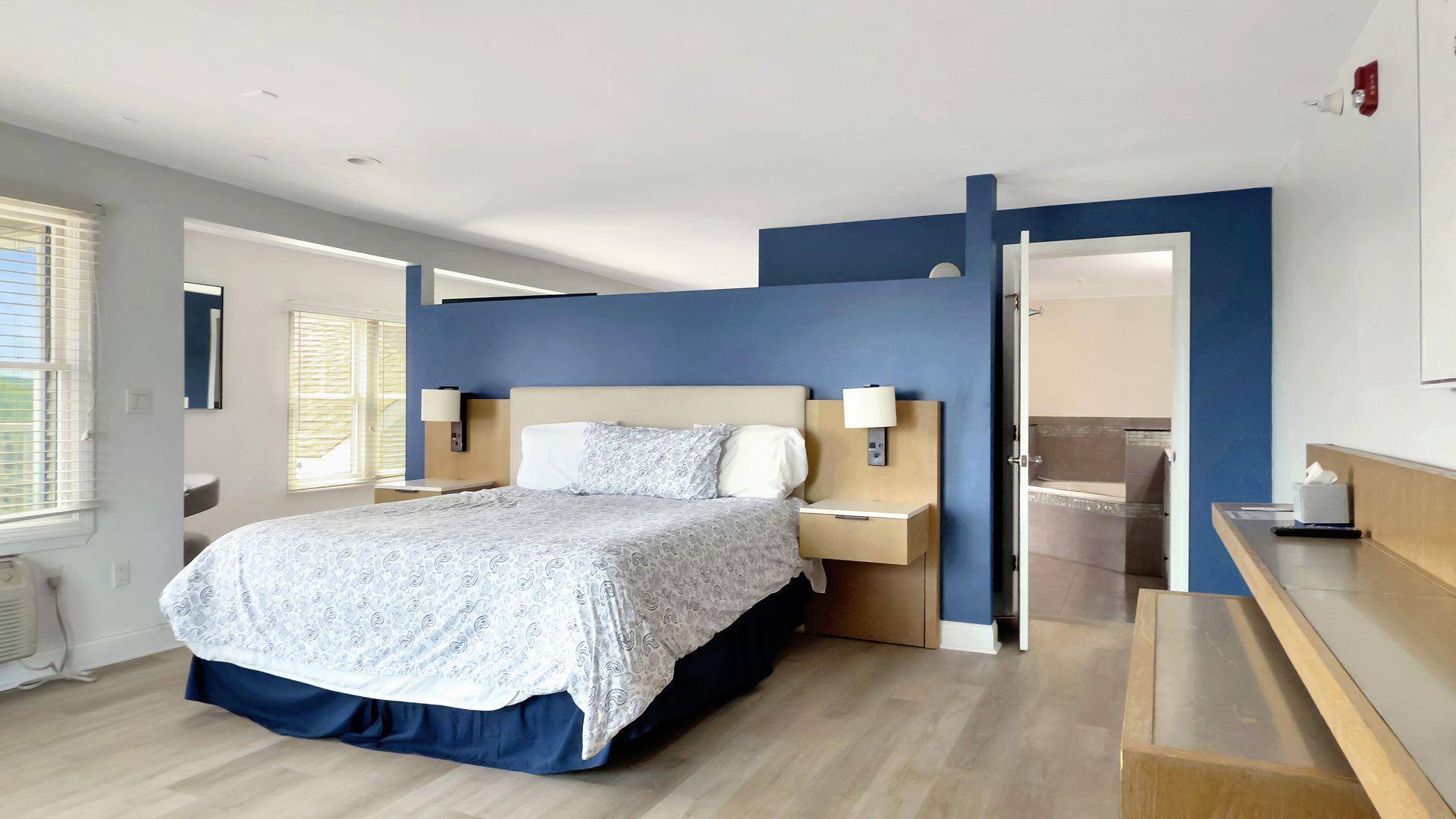 Spacious hotel room with a blue accent wall, bed, and a doorway to a bathroom.