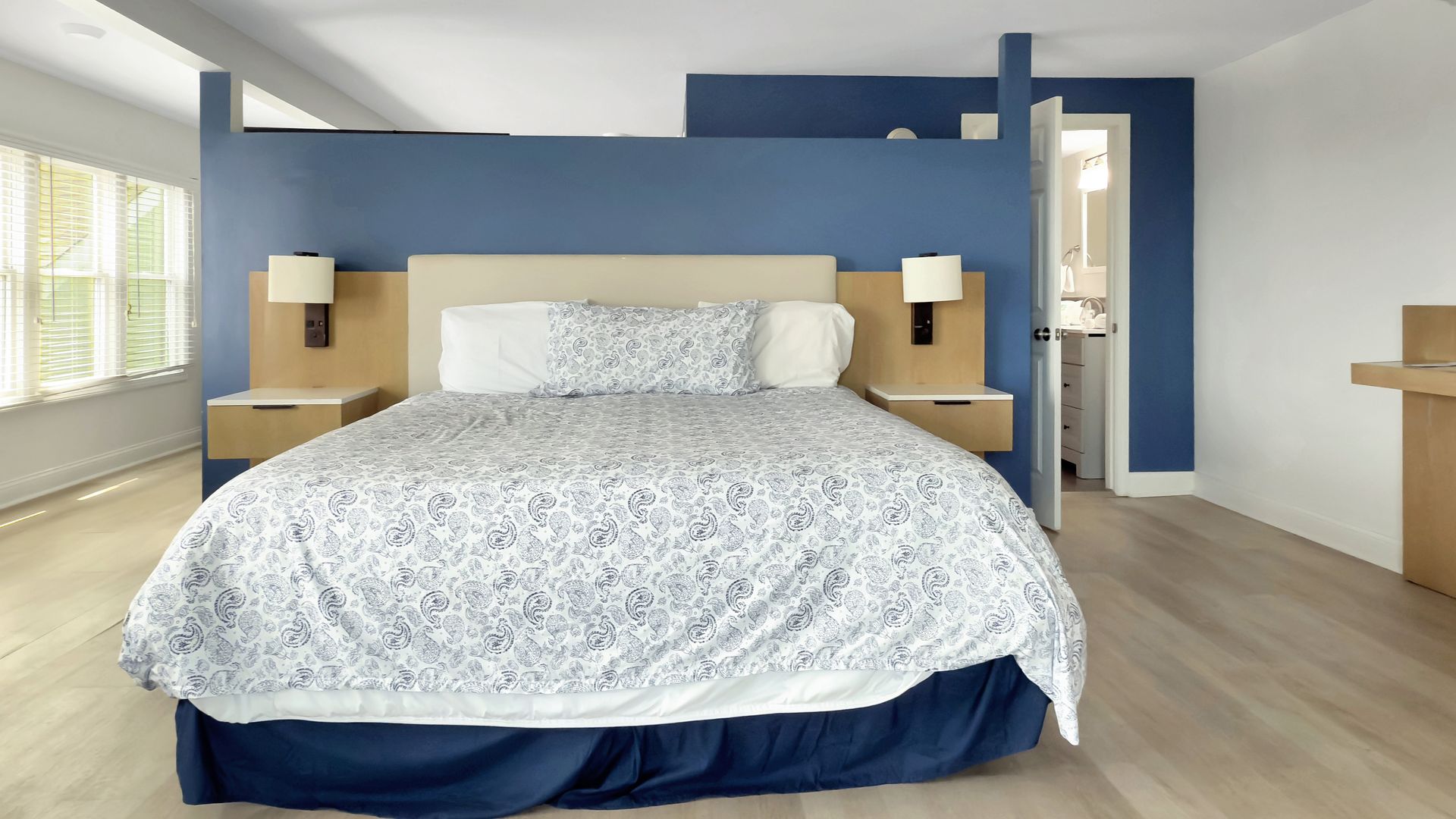 Bedroom with blue wall, bed with patterned duvet, bedside tables, and a doorway.