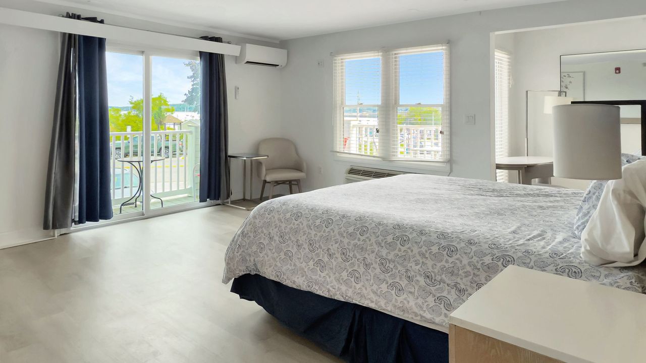 Bright bedroom with king bed, balcony access, and large windows overlooking an outdoor view.