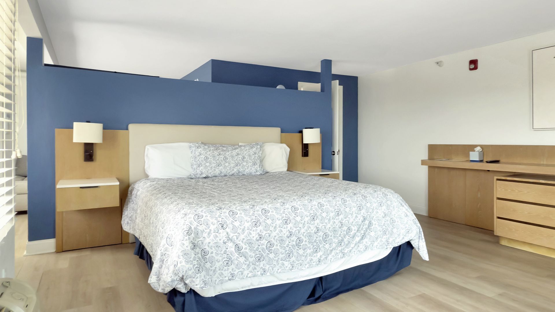 Bedroom with a blue accent wall, bed, nightstands, desk, and light-colored wood floor.