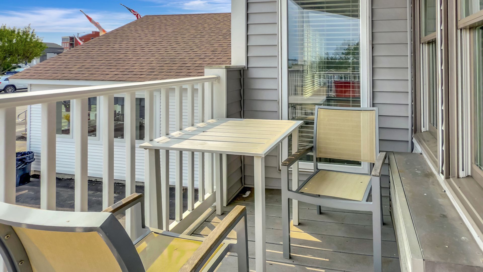 A small balcony with a table and chairs, overlooking a street and buildings.