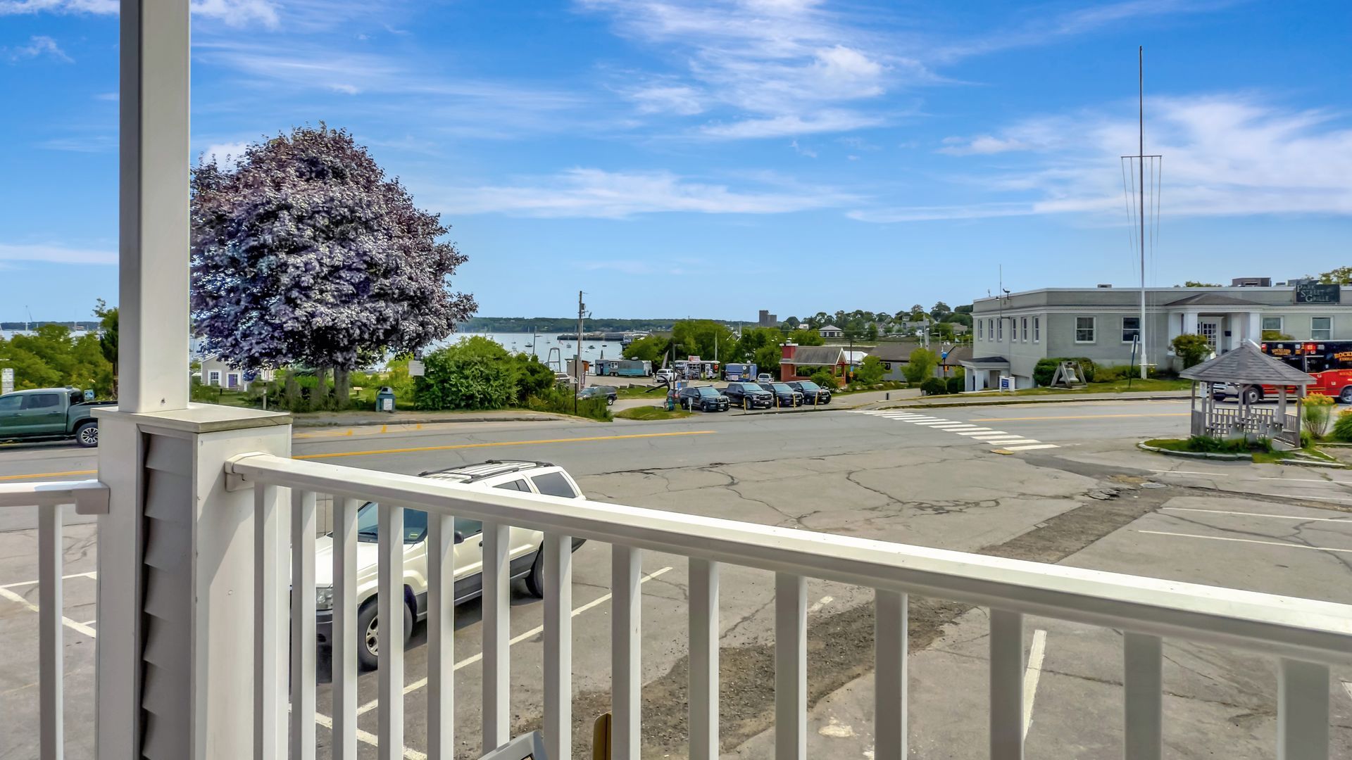 View from a porch overlooking a parking lot, town, and water under a blue sky.
