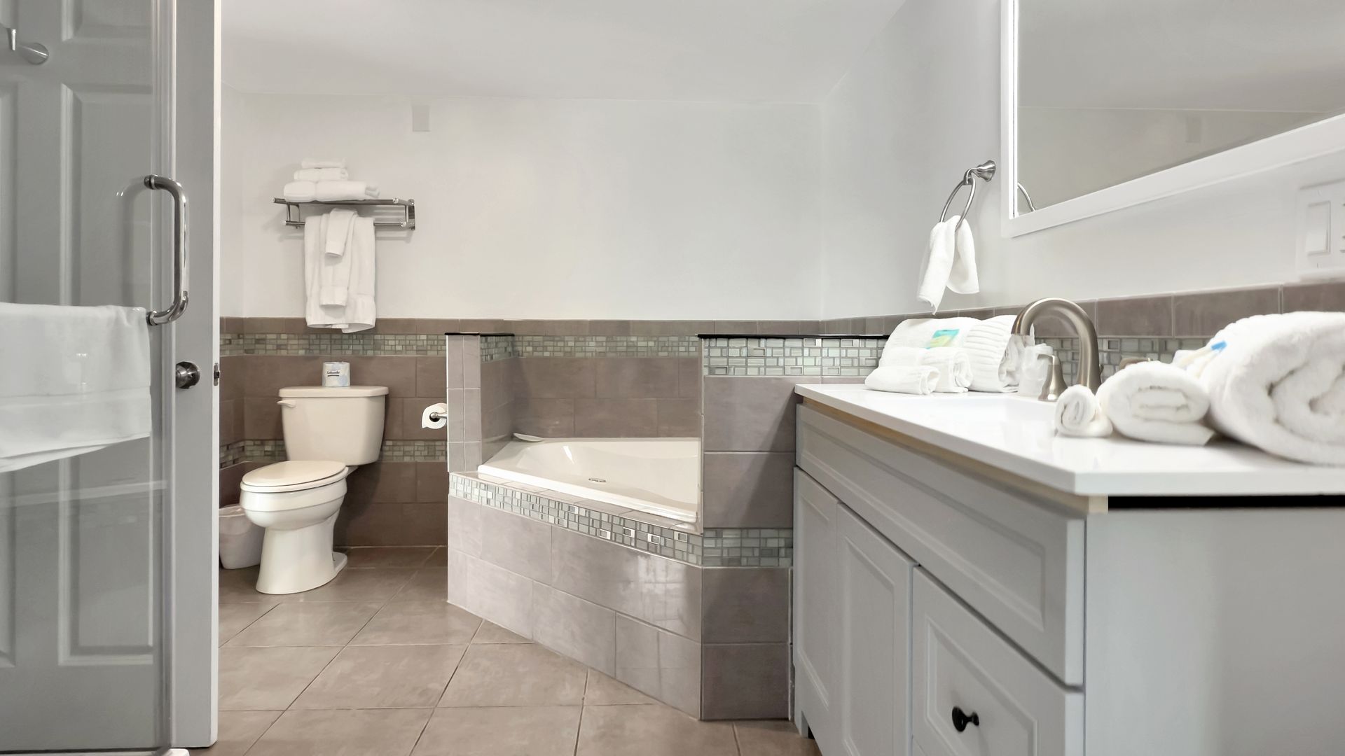 Bathroom with white cabinets, toilet, and a built-in tub with grey tile.