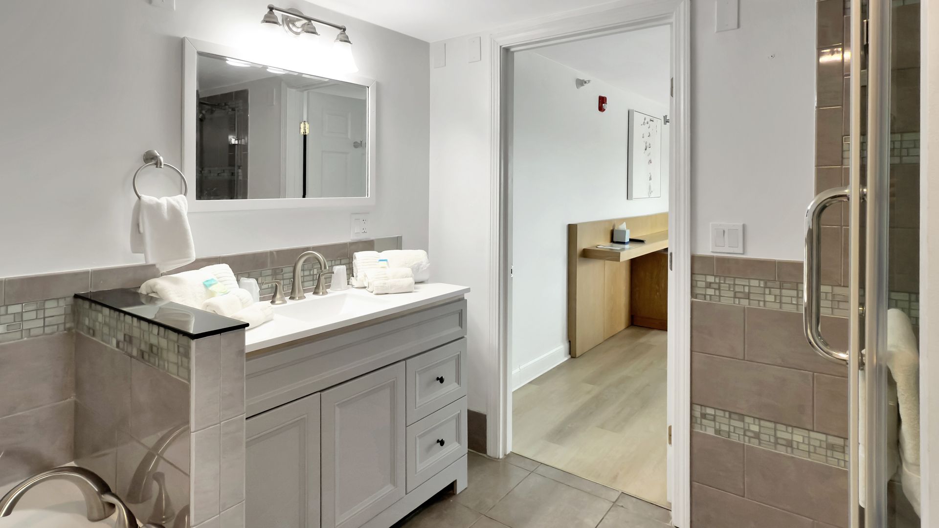Bathroom with vanity, mirror, and doorway to another room. Gray and white tones.