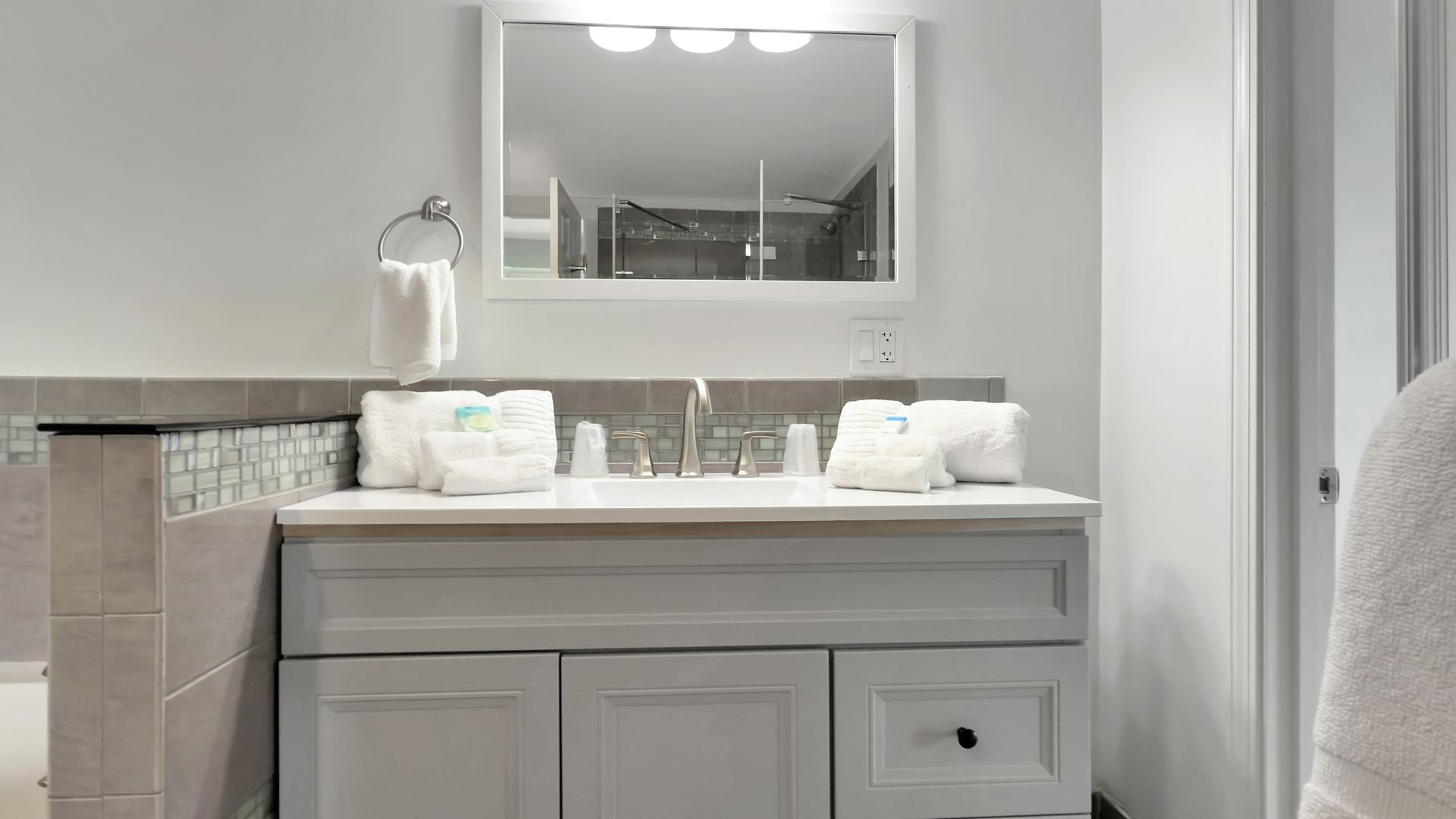 Bathroom with a light gray vanity, marble countertop, and a mirror with overhead lights.