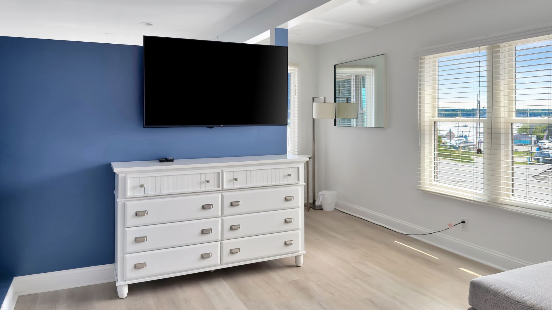 White dresser and TV against blue wall, next to a window overlooking water.