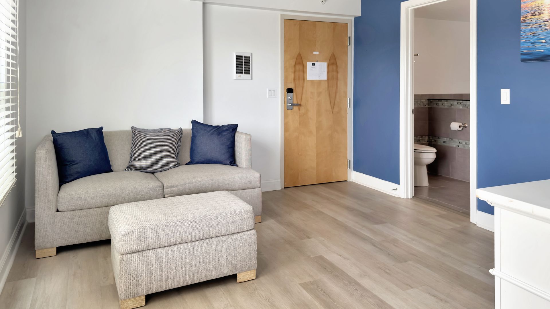 Living room with sofa, ottoman, door to bathroom, and blue accent wall.