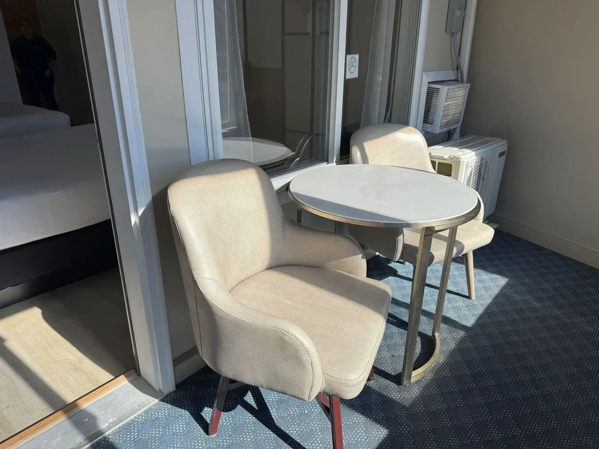 A hotel room balcony with two chairs, a small table, and a mirrored wall. Blue carpet, beige tones.