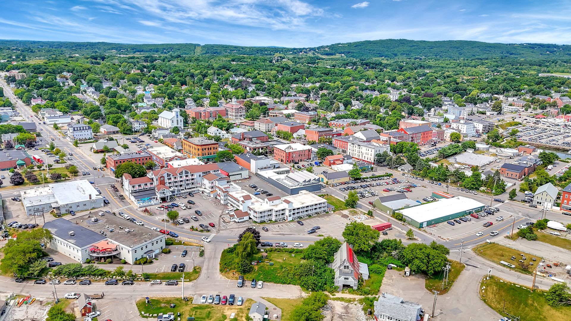 Aerial view of a town with buildings, roads, and greenery under a bright blue sky.