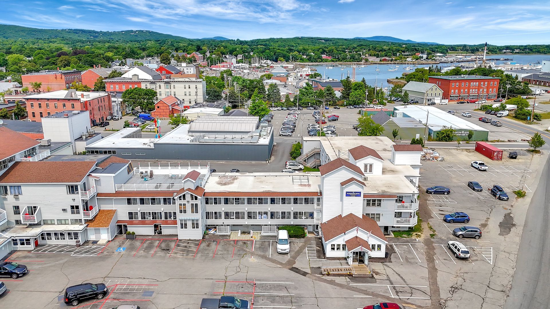 Aerial view of a downtown area with buildings, parking, and a waterfront in the background.