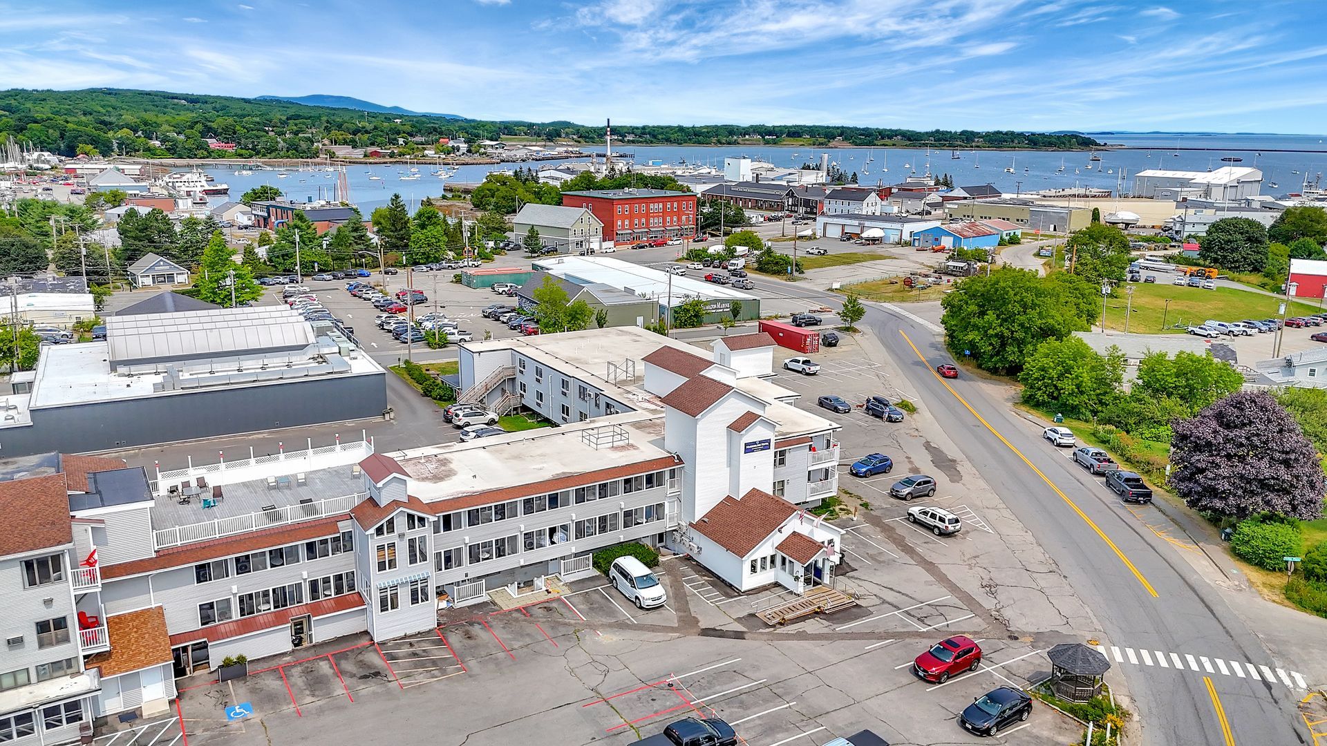 Aerial view of a coastal town with buildings, cars, and a harbor under a blue sky.