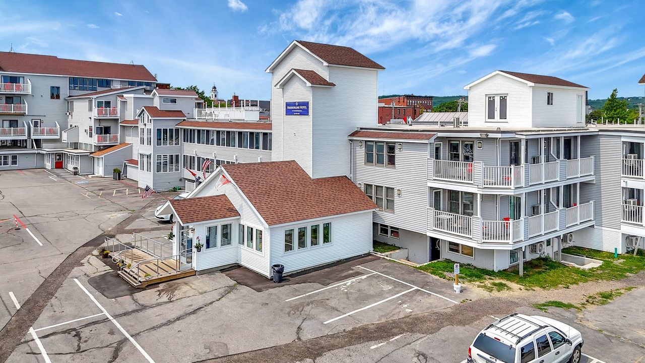 White motel with a red roof, a tower with a blue sign, and a parking lot.