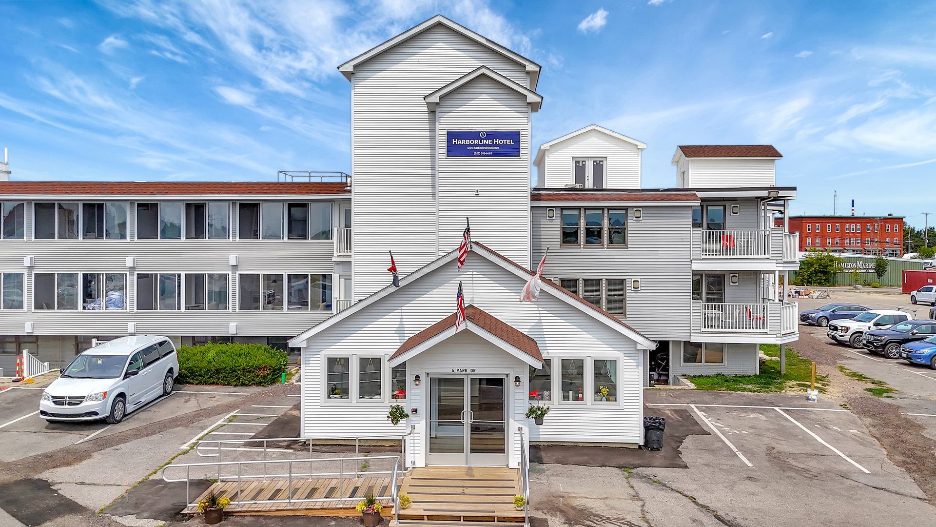 White building with multiple stories, entry with peaked roof, cars parked outside.