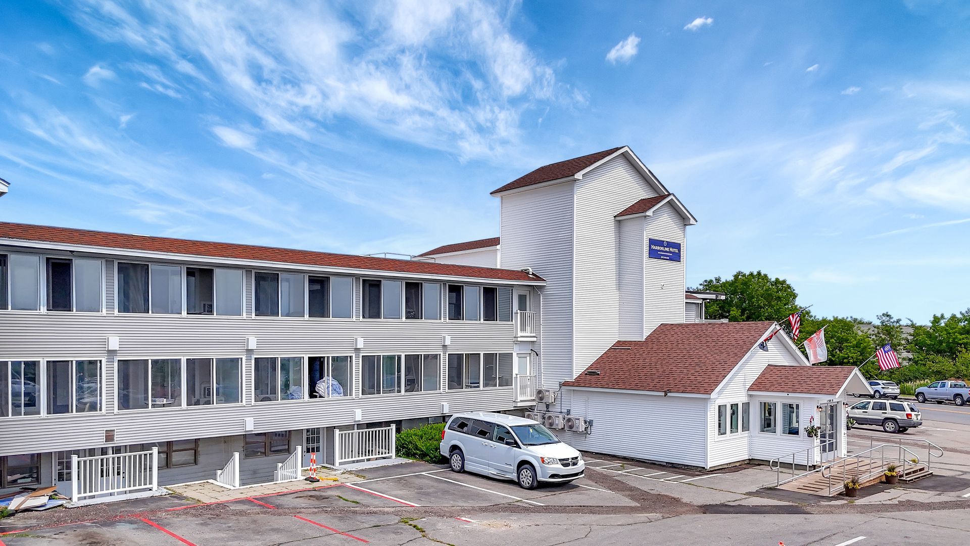 White hotel building with brown roof and a white van parked out front. Blue sky.