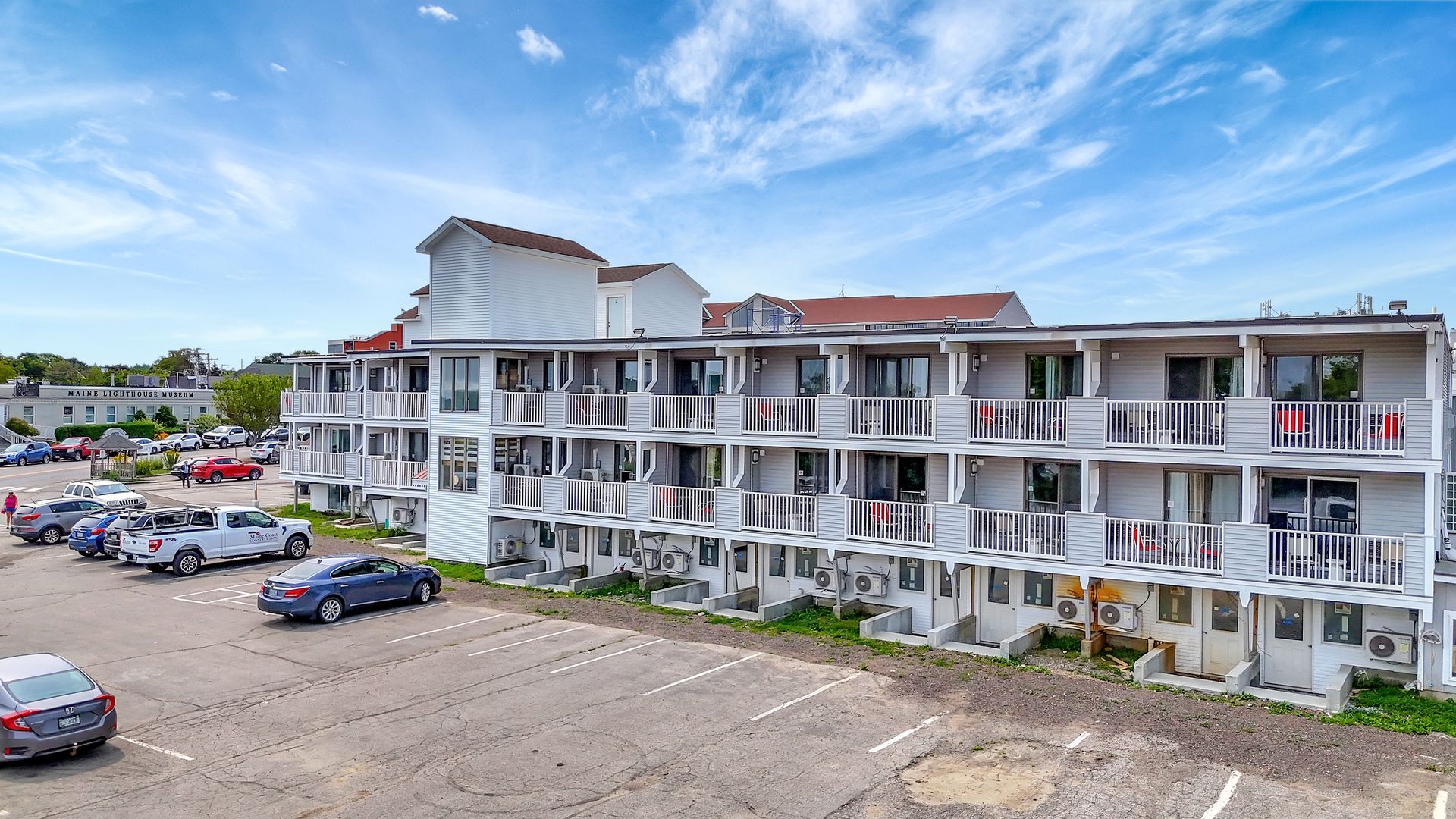 Multi-story building with balconies and many air conditioning units; parked cars in front.