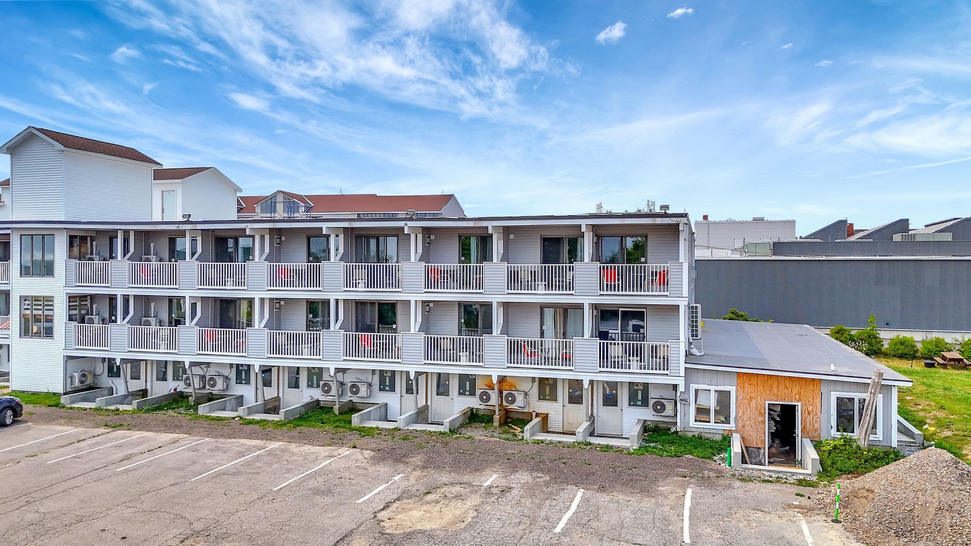 Multi-story gray building with balconies; parking lot in front; sunny day.