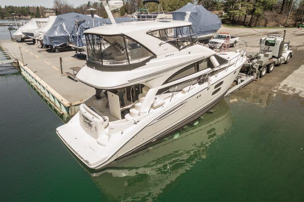 A boat is being towed by a semi truck in a marina.