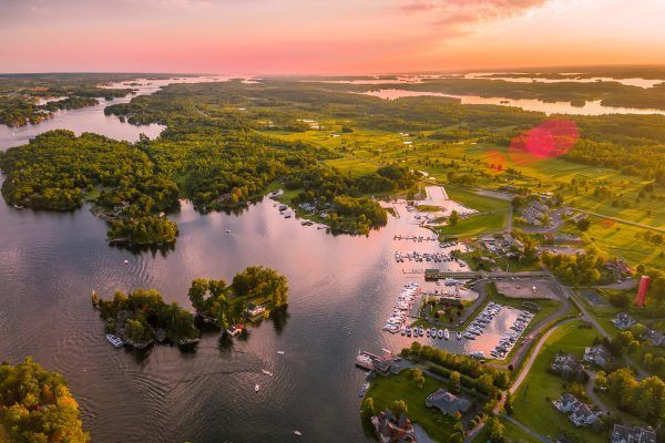An aerial view of a lake surrounded by trees and houses at sunset.